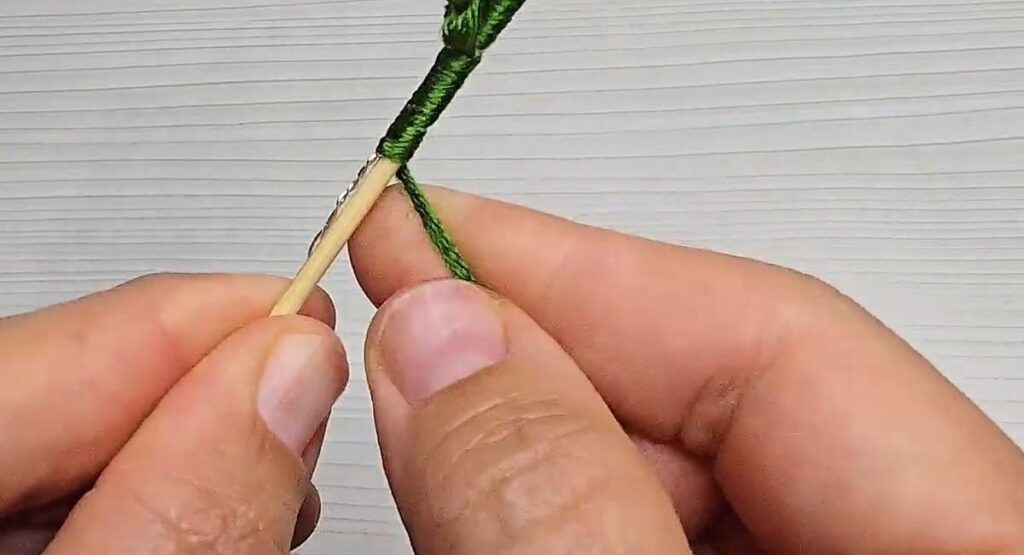 Twisting the leaf wire around the wrapped stem of a crochet rose with stem