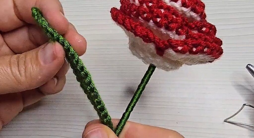 Side view of the crochet rose with stem showing white petals and red edges