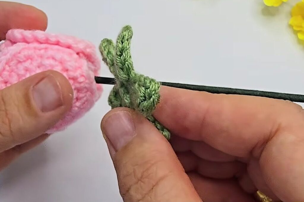 Green calyx threaded onto the stem below the crochet rosebud