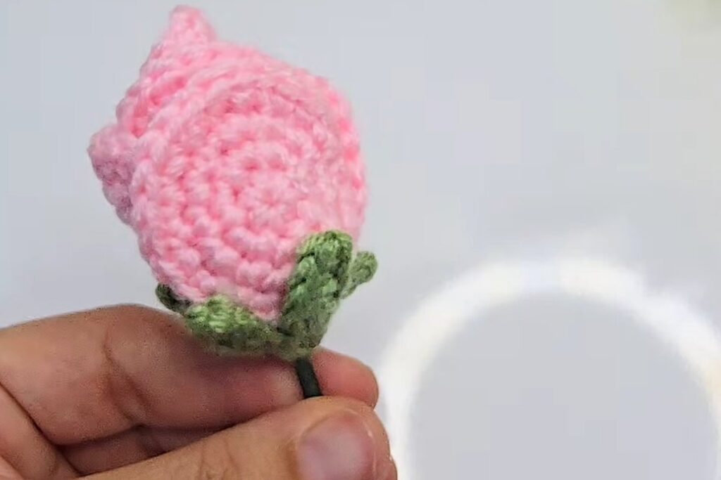 Finished pink crochet rosebud with a green five-point calyx on a green stem