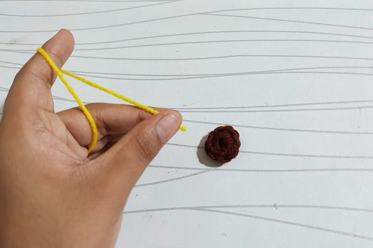 A small brown crochet disc fastened off next to yellow yarn