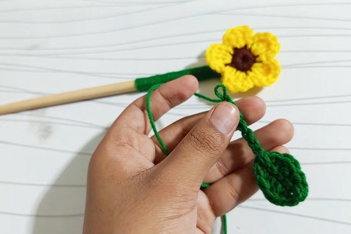 Small crocheted green leaf held next to the sunflower stick