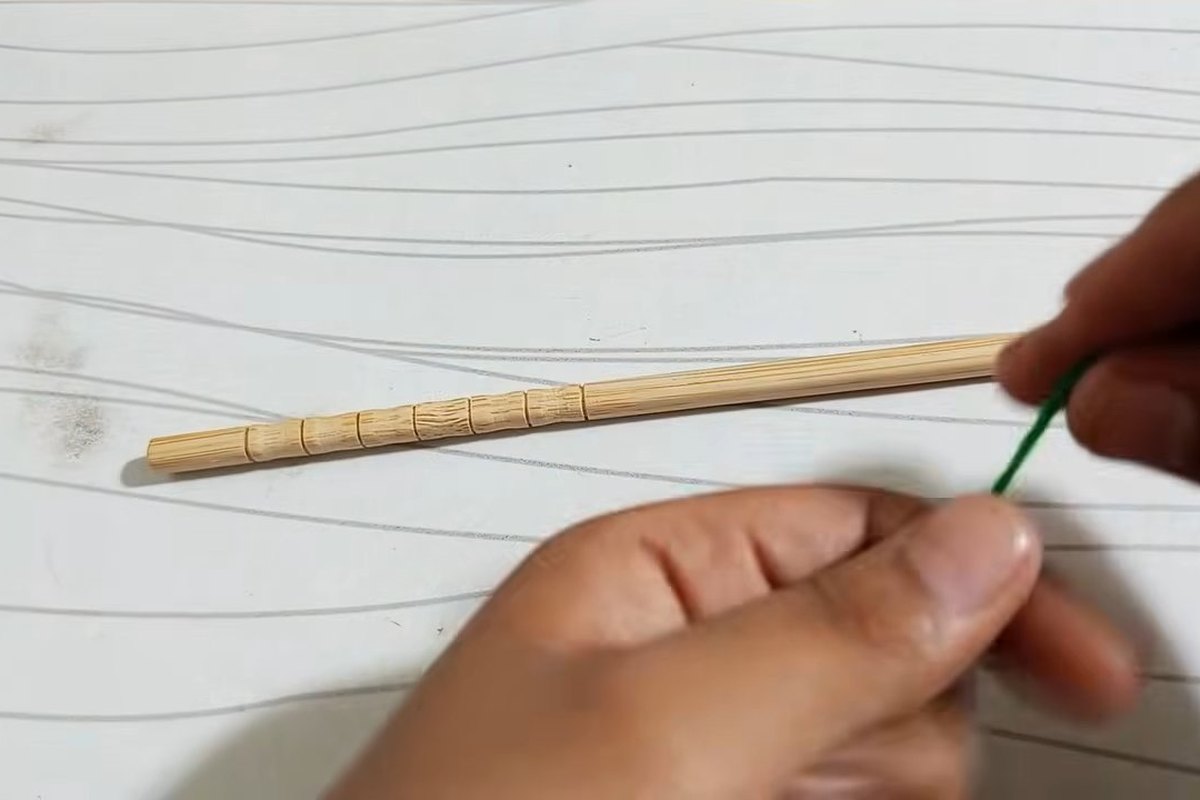 Wooden stick with a strand of green yarn laid beside it