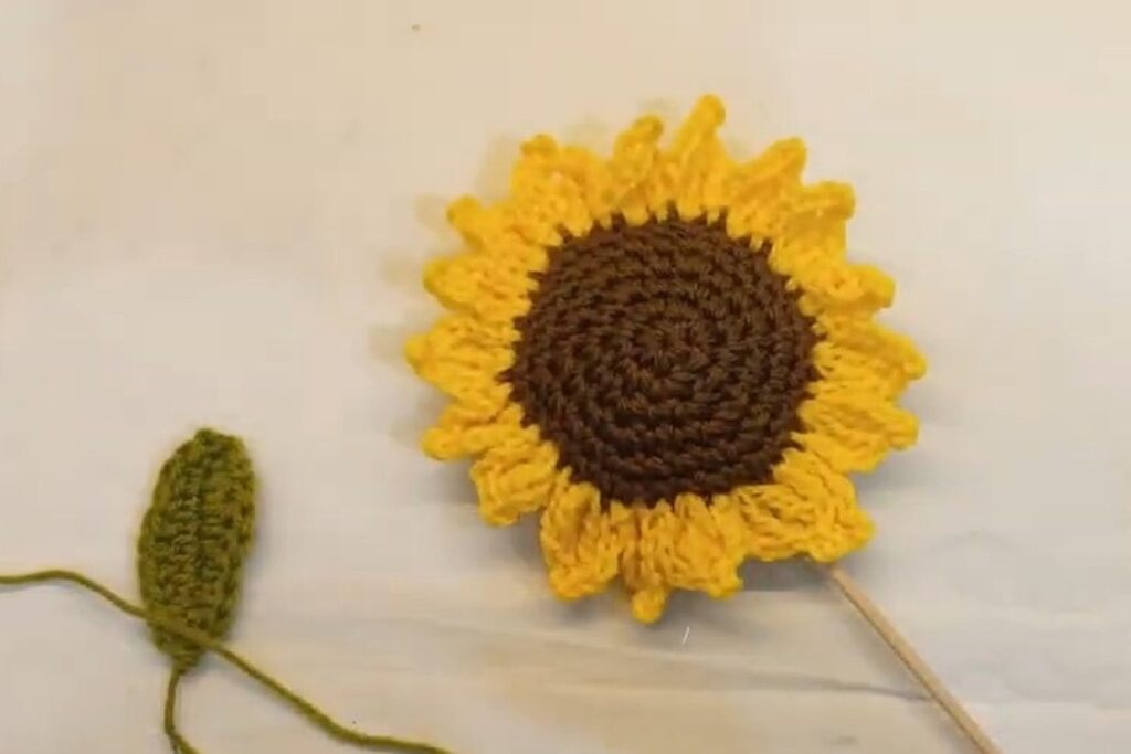 Finished crochet sunflower pattern with a brown centre, 18 yellow picot petals and a crochet leaf