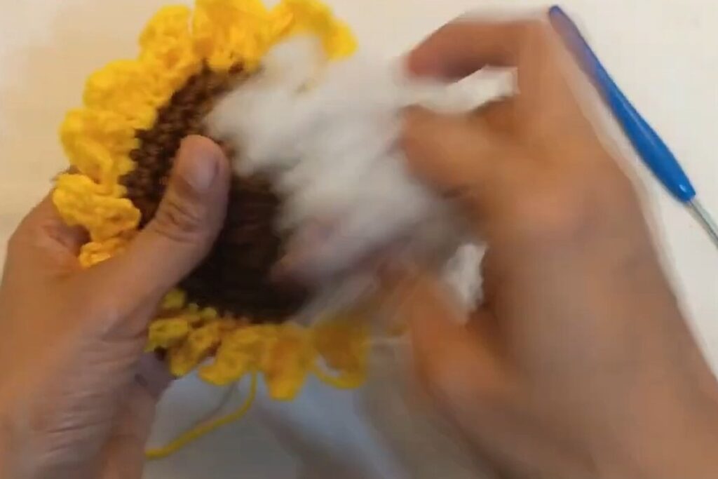 Stuffing the crochet sunflower with fiber fill before closing