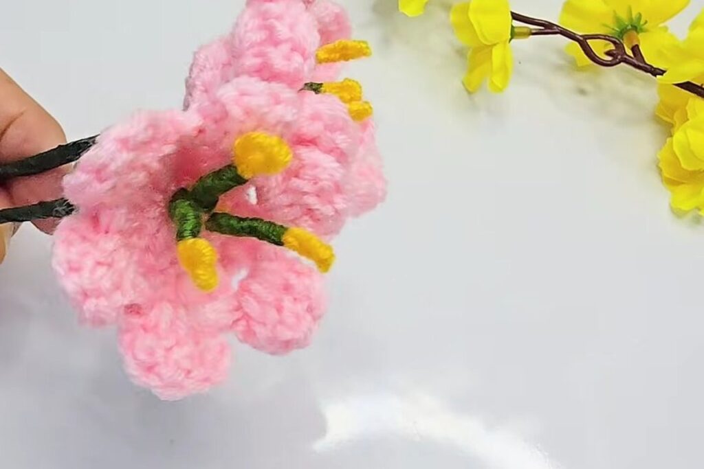 Close-up of one pink crochet blossom with two petal tiers and yellow wire stamens