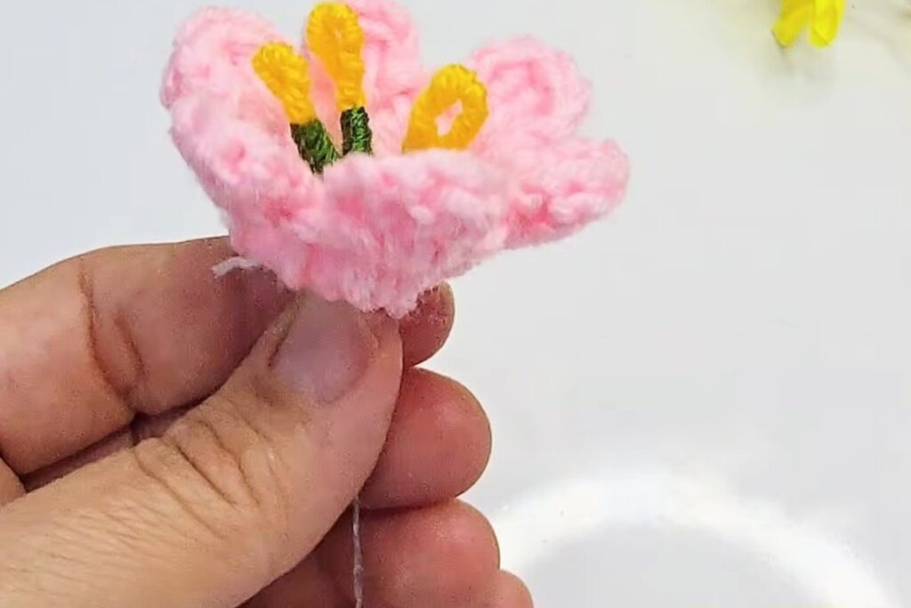 Pink crochet blossom with three yellow stamens standing in the centre