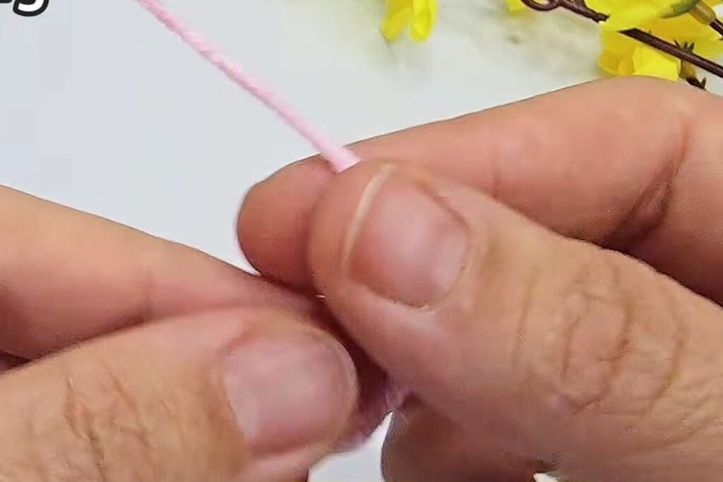 Pink yarn wrapped around the fingers to make a magic ring