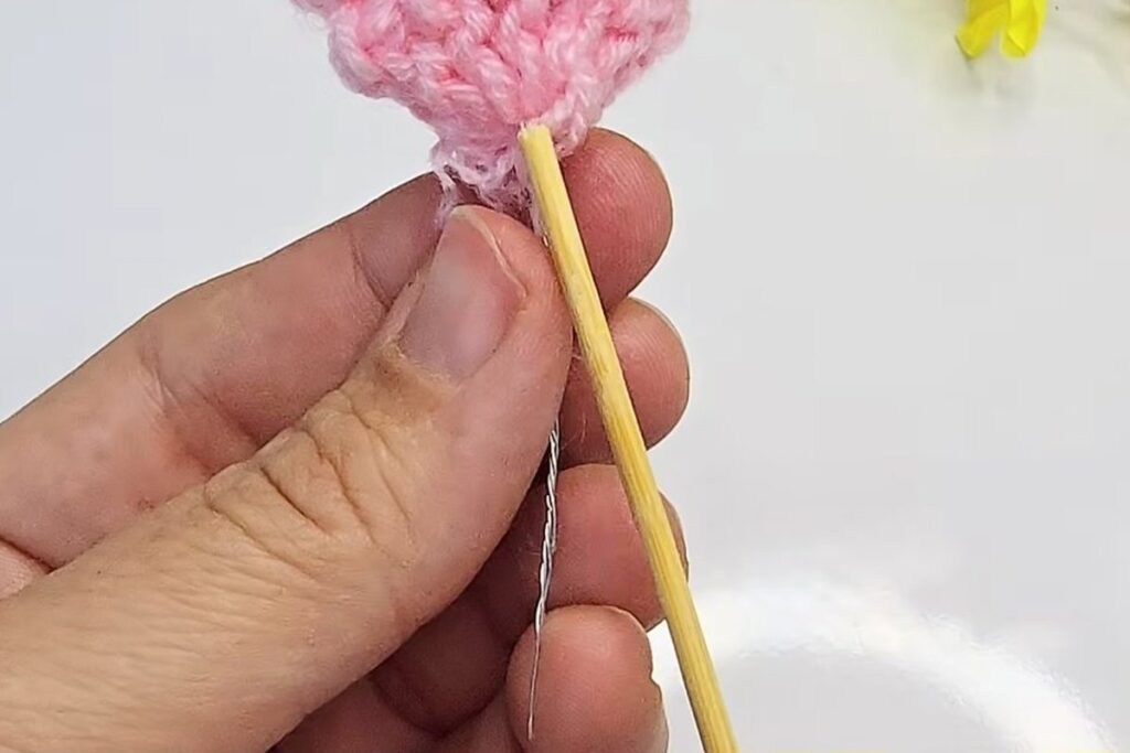 Wooden toothpick pushed into the base of the crochet blossom next to the wires