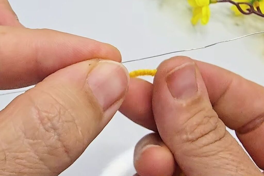 Thin craft wire held next to a short piece of yellow yarn