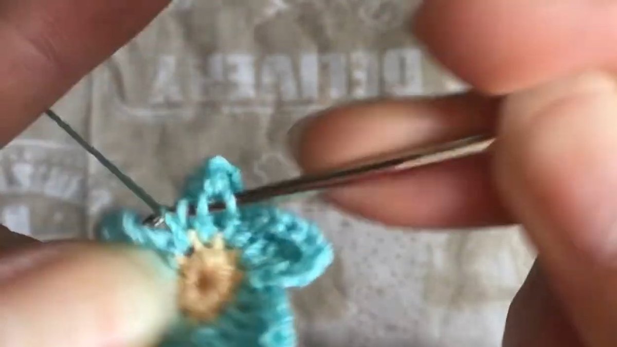 Five teal petals round the peach centre with the hook finishing the last petal of the crochet forget me not flower