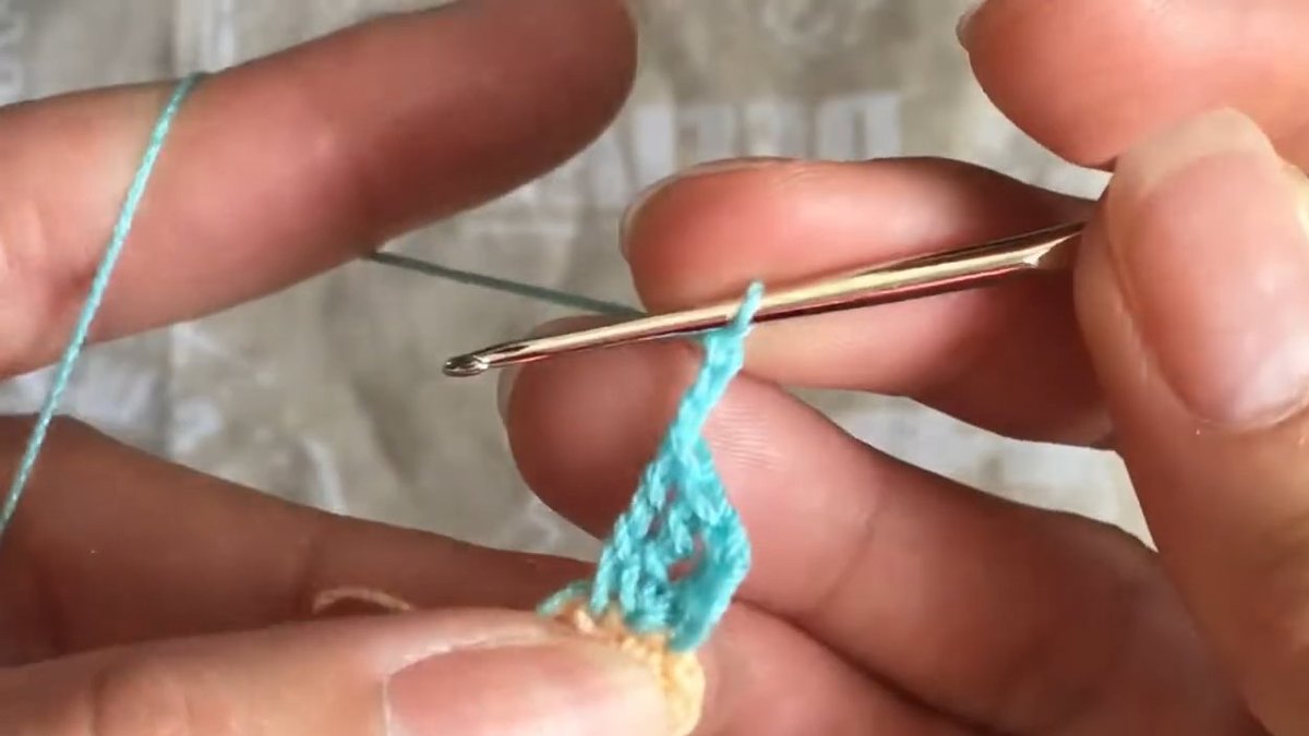 First finished teal petal lying flat against the peach centre with the hook ready for the next petal of the crochet forget me not flower