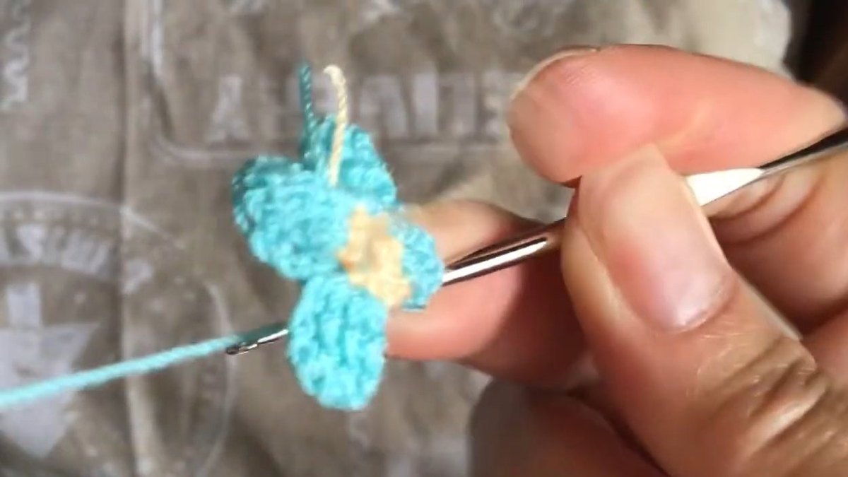 Four teal petals round the peach centre seen from above with one gap left for the crochet forget me not flower