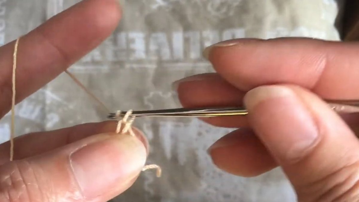 Steel hook pulling peach thread through a small loop at the start of the crochet forget me not flower