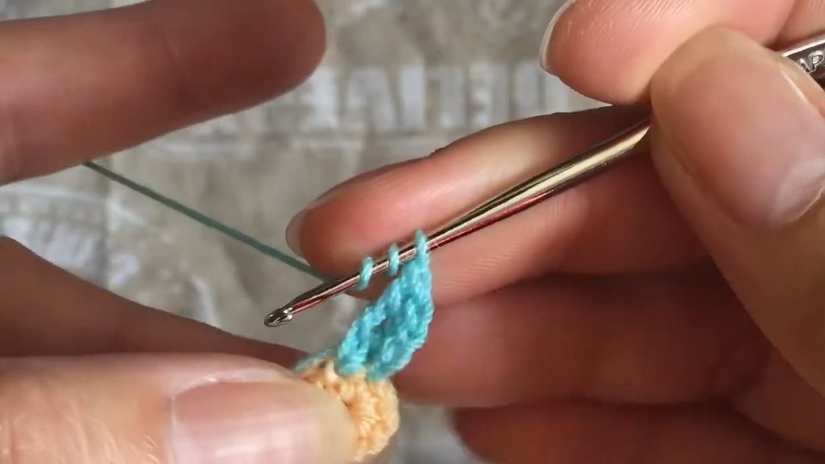 Narrow teal oval petal standing up from the peach centre with the hook beside it for the crochet forget me not flower