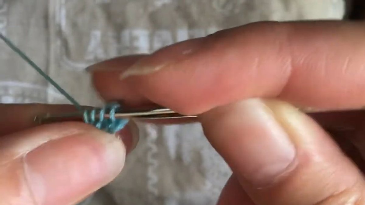 Several teal loops standing in a row on the hook above the peach disc while working a crochet forget me not flower petal