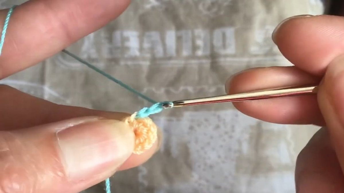 Teal thread started on the edge of the peach disc with the hook ready for the first petal of the crochet forget me not flower
