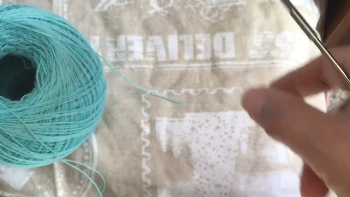 Ball of teal thread beside a hand holding a crochet hook before starting the crochet forget me not flower