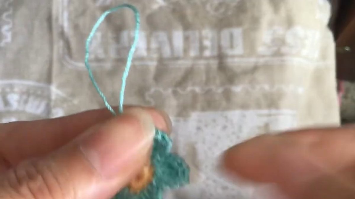 Teal thread held up in a loop above the finished crochet forget me not flower