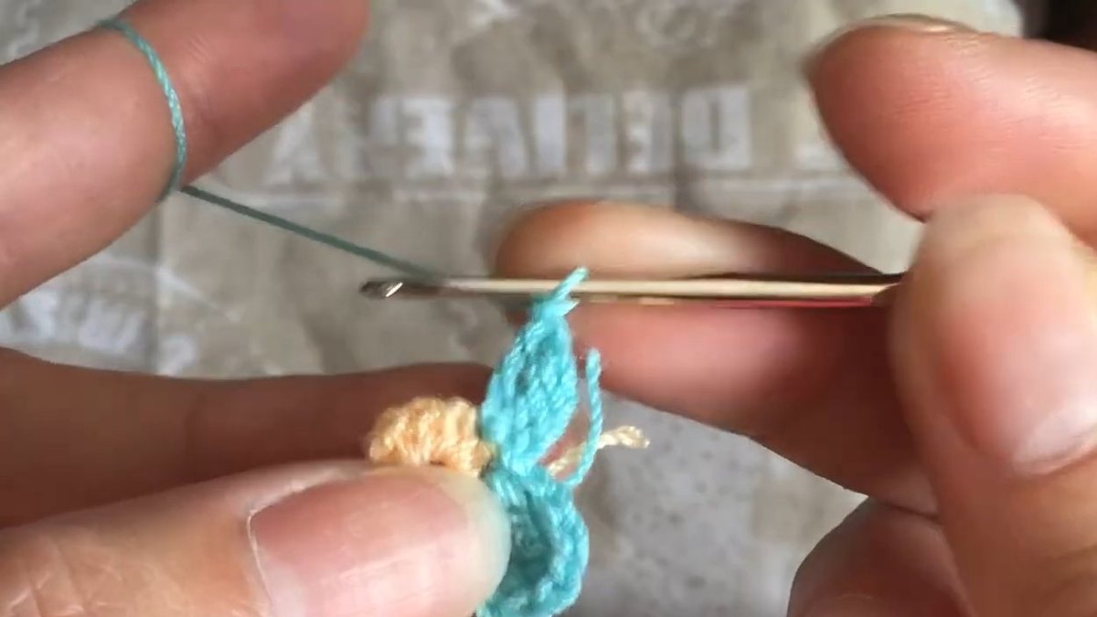 Three teal petals around the peach centre with the hook pointing to the gap for the fourth petal of the crochet forget me not flower