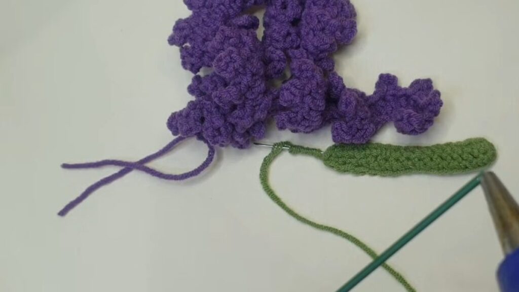 Coiled purple strip, green leaf, green floral stem and glue gun ready to assemble a crochet lavender flower