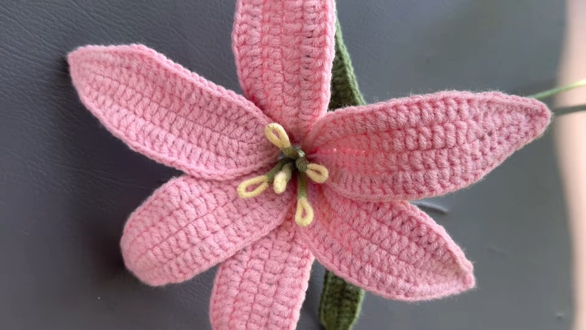Finished crochet lily flower with six pink petals, yellow stamens and a green leaf