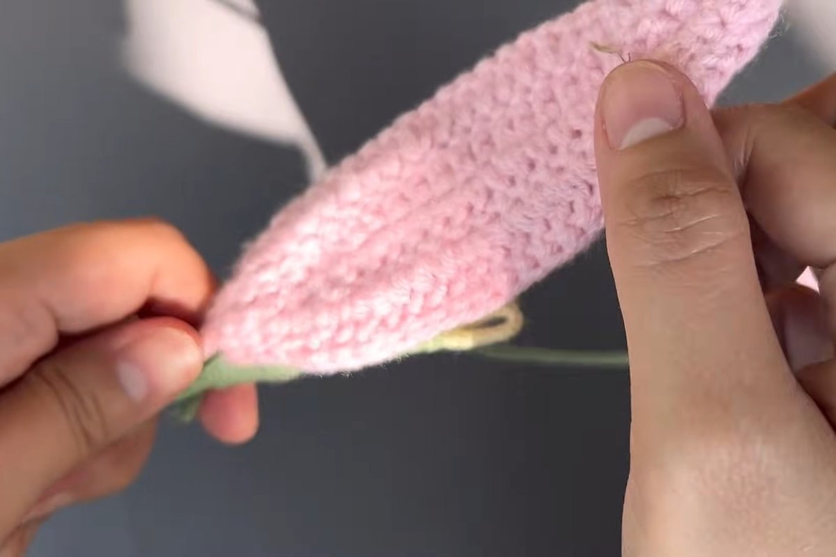Pink crochet petal being held against the stamen bundle of a crochet lily flower