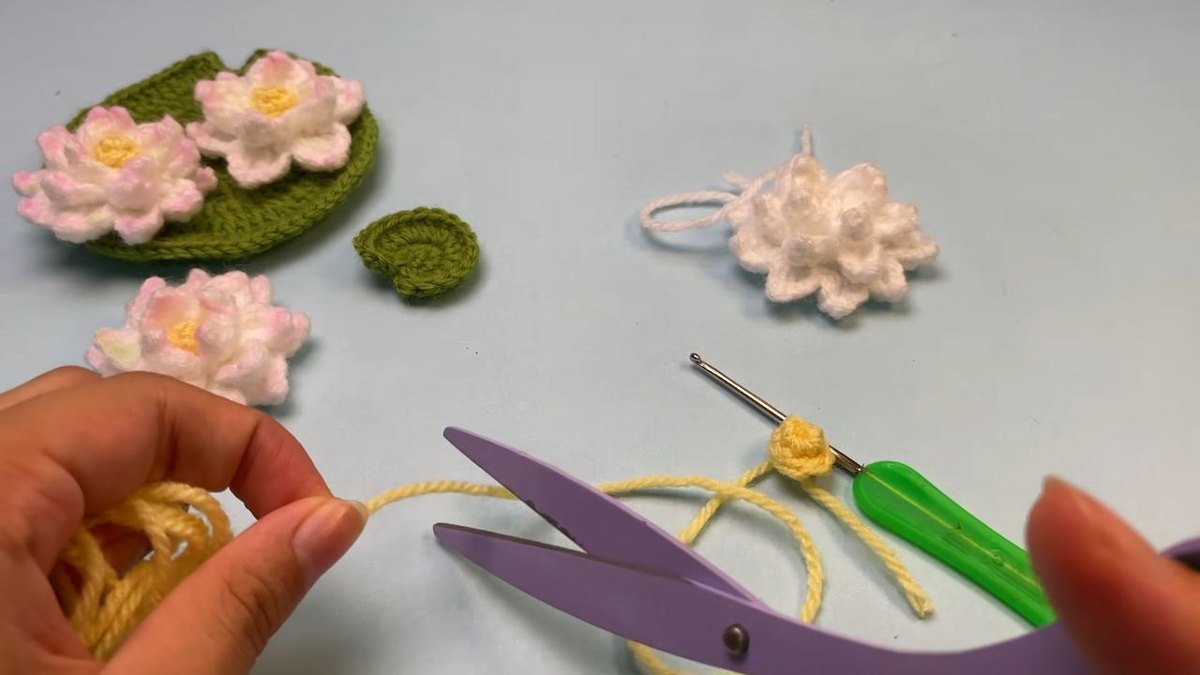 Small finished yellow ball beside a hook for the centre of a crochet lotus flower