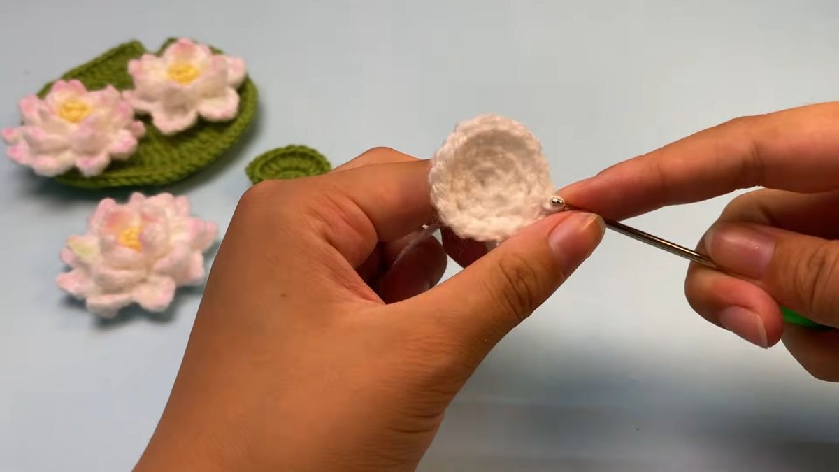 Flat round disc of white crochet held in one hand after round 3 of a crochet lotus flower