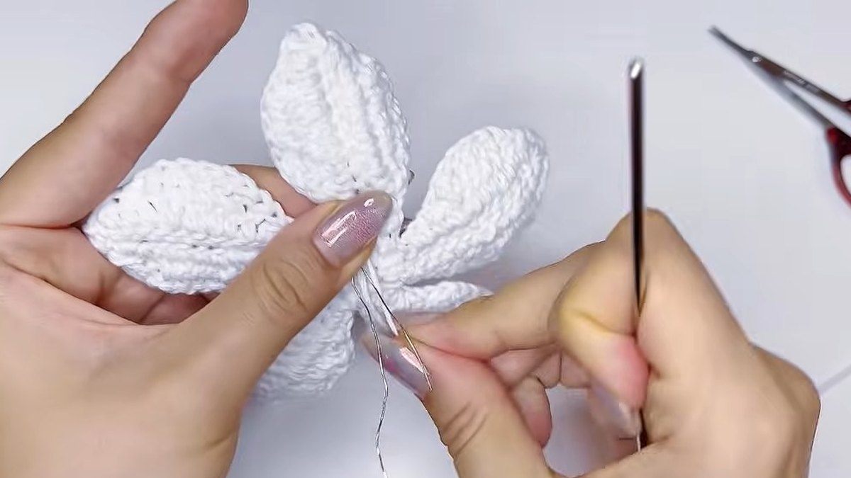 Small white crochet flower with five petals held up with a pair of scissors beside it