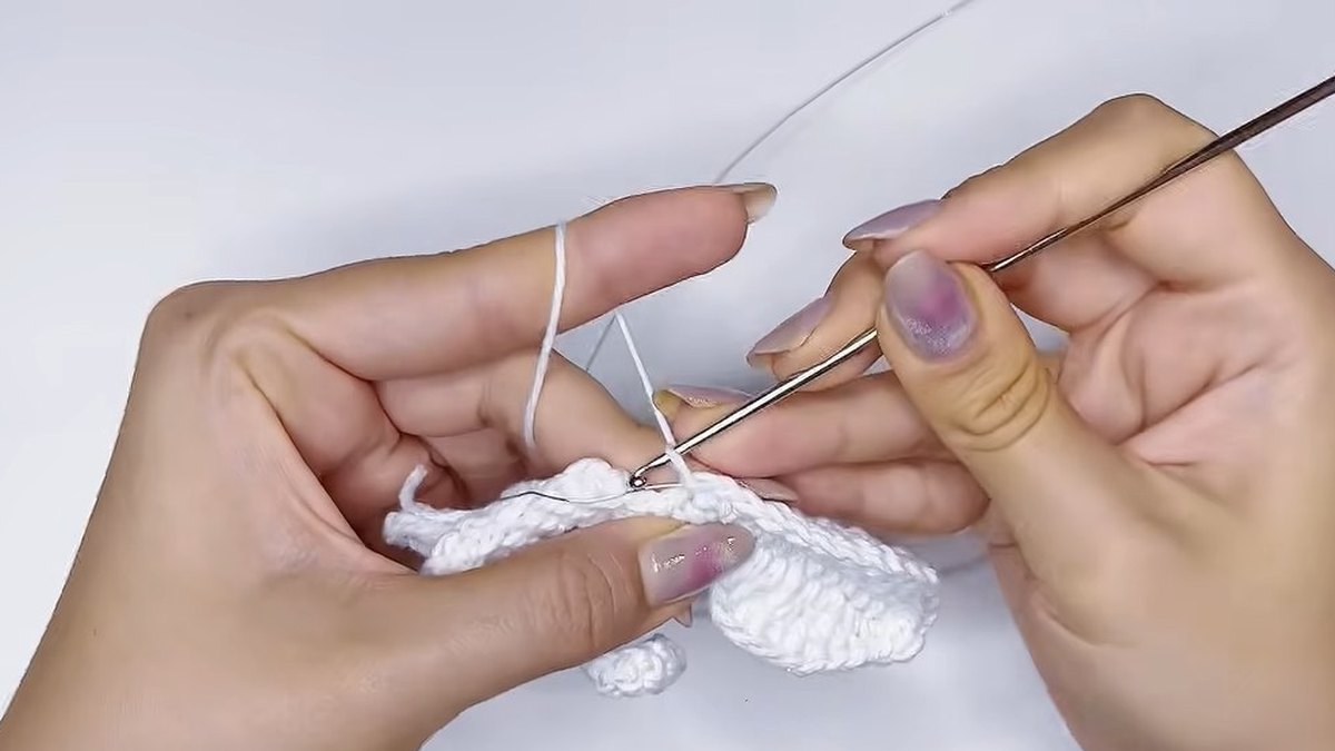 Finished white crochet petal with its wire along the edge, held next to the unworked strips of the small crochet magnolia flower