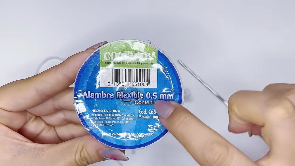 Hand holding a blue spool of flexible floral wire labelled 0.5 mm next to a small crochet hook