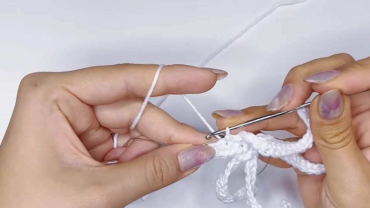 Hook shaping the first side of a long white petal over the wire in the large crochet magnolia flower