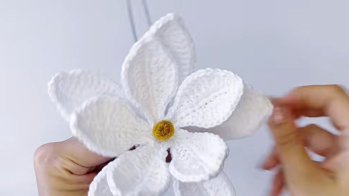 Crochet magnolia flower with large white petals sitting between the small petals around a gold centre