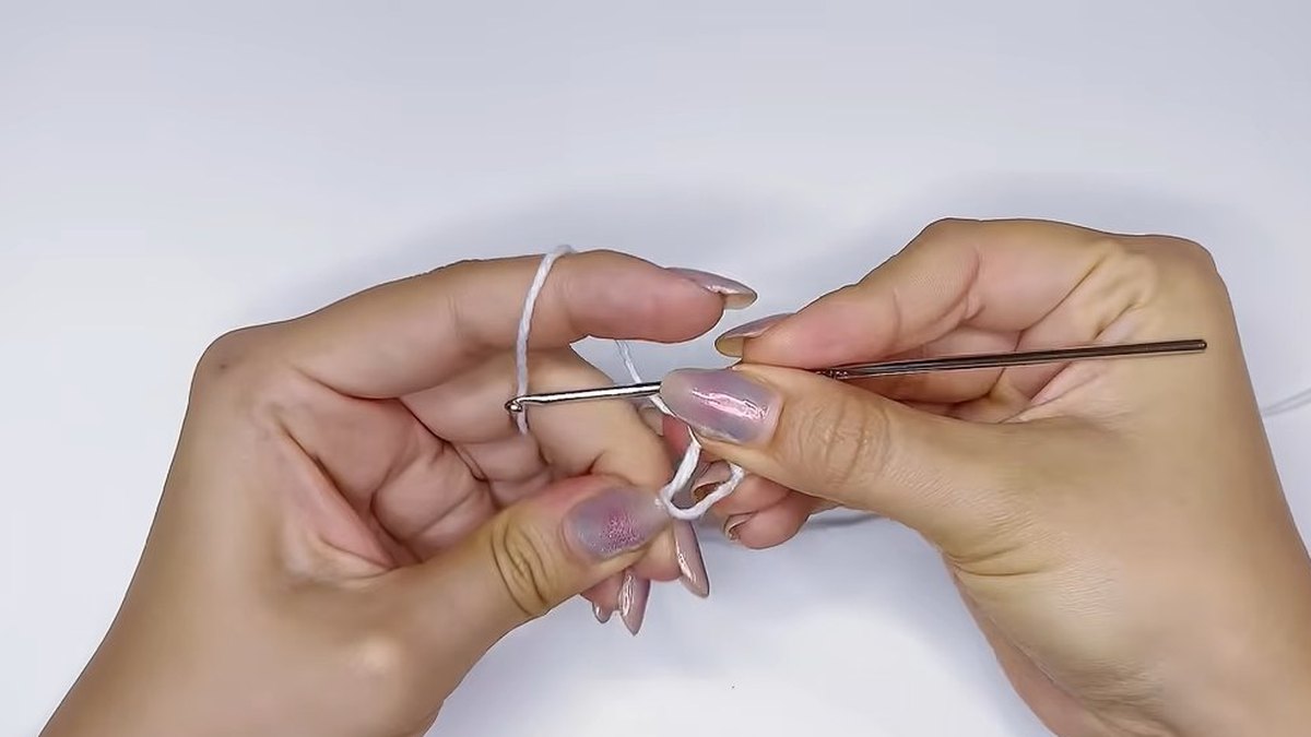 Hook and fingers closing a magic ring of white thread to start the small crochet magnolia flower