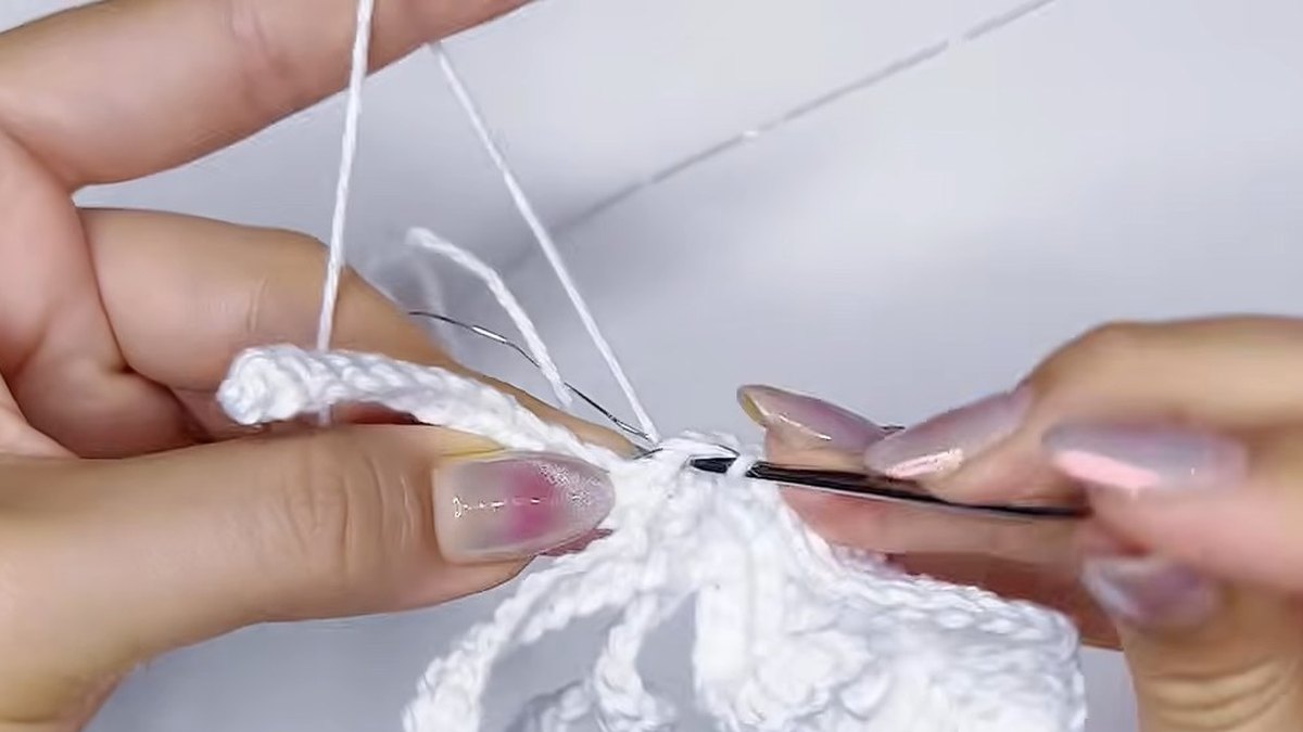 Thread lying in front of the wire as the hook moves from one white petal to the next in the small crochet magnolia flower