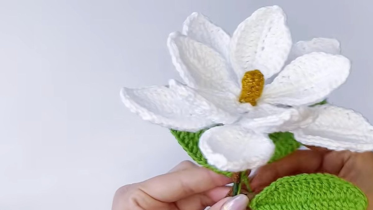 Green crochet leaves being placed against the wrapped stem below the crochet magnolia flower