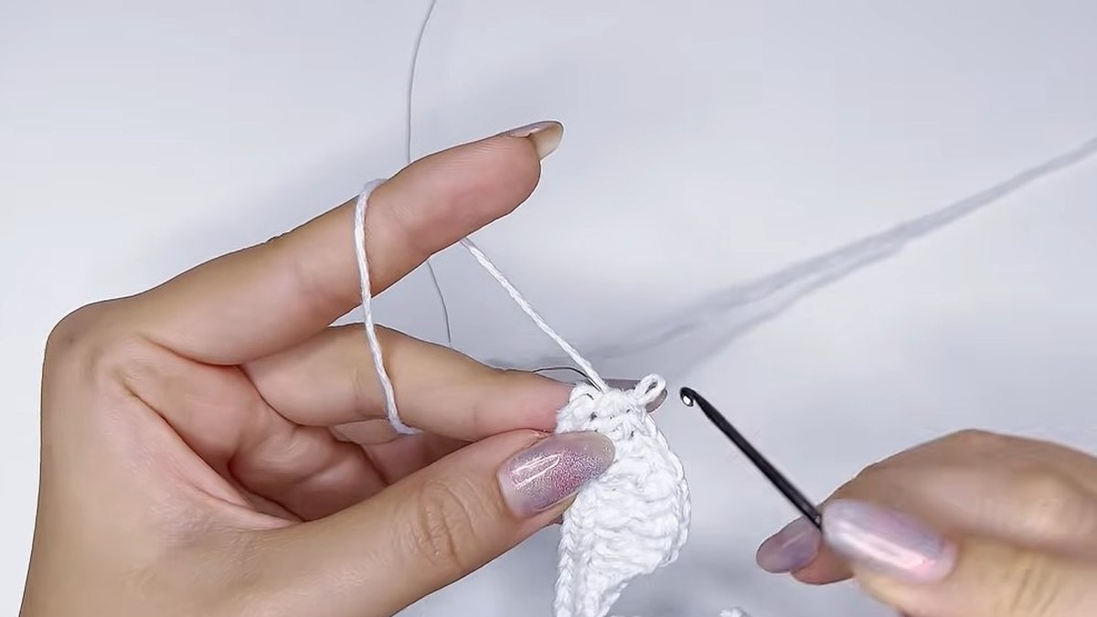 Hook working the tip of a white petal with the wire lying beside it in the small crochet magnolia flower
